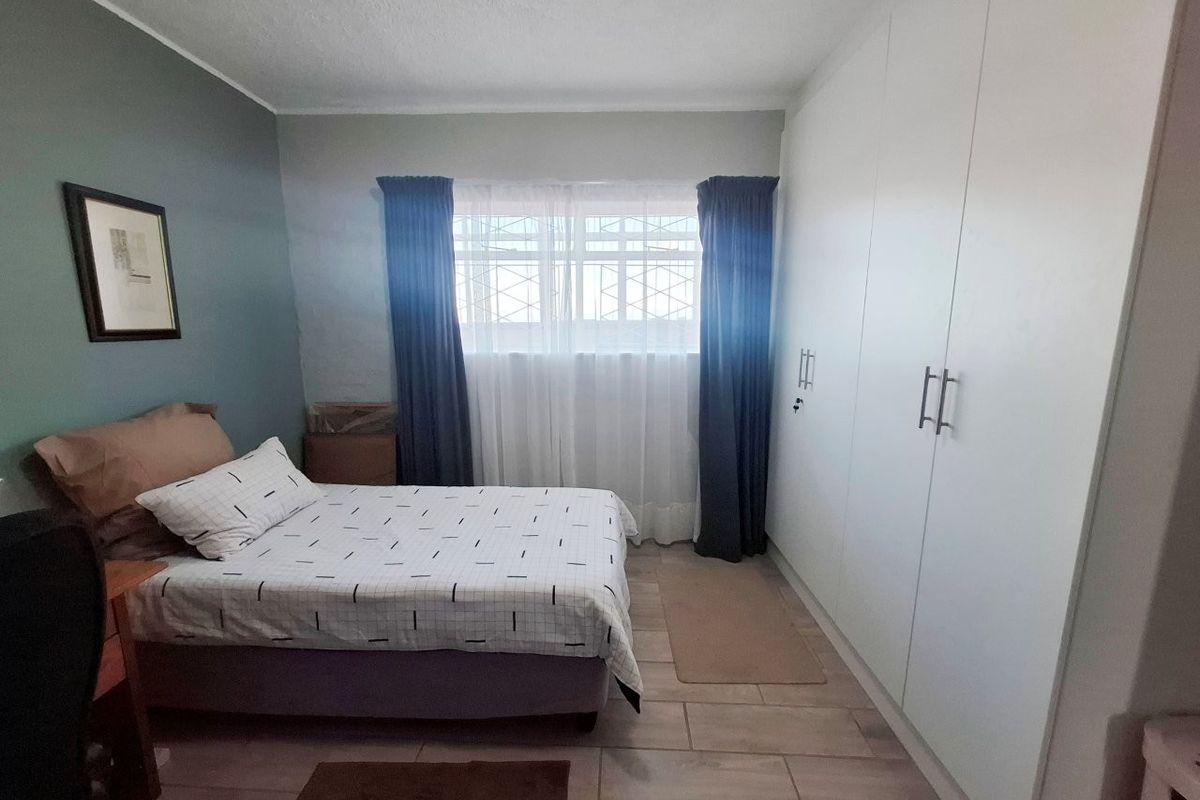 A well-maintained bedroom featuring built-in cupboards, tiled flooring, and security bars on the window.