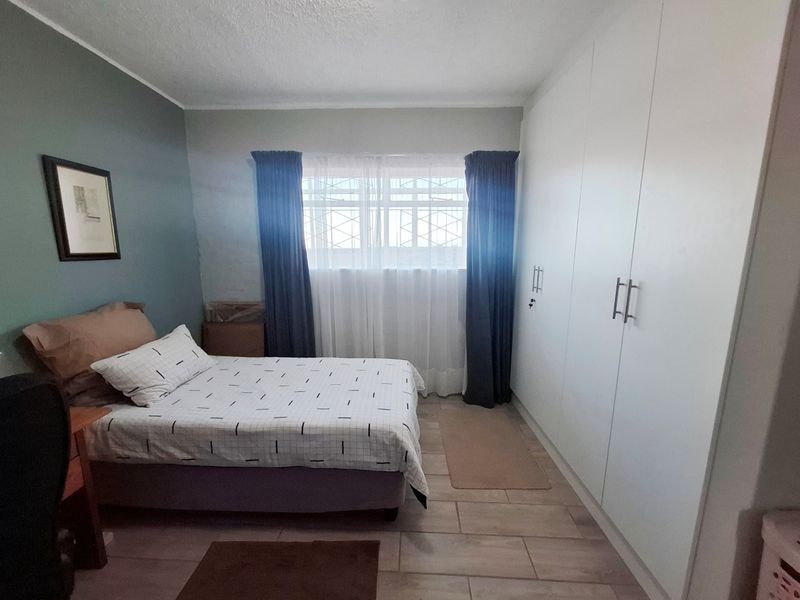 A well-maintained bedroom featuring built-in cupboards, tiled flooring, and security bars on the window.