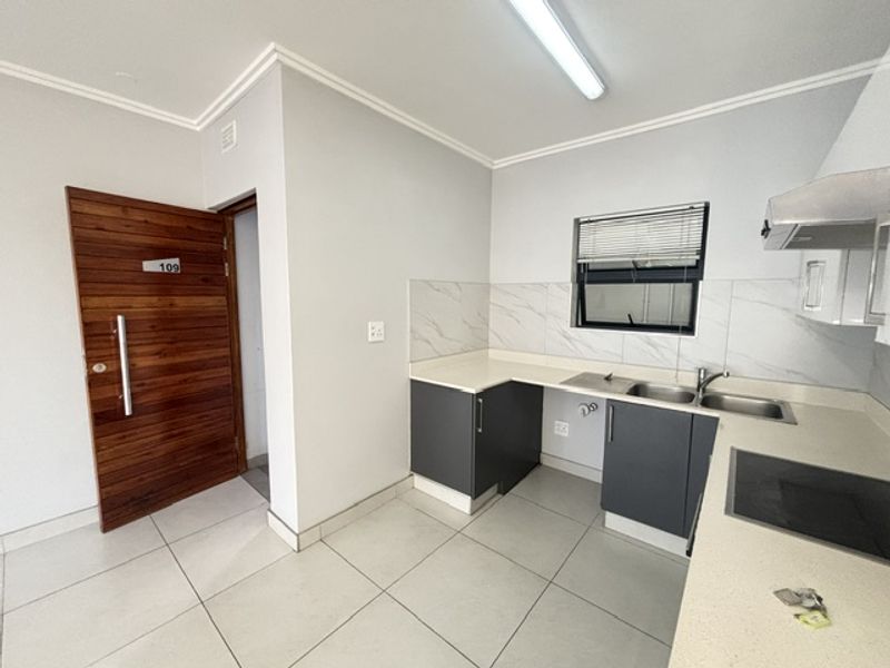 Modern kitchen featuring dark grey cabinetry, stone countertops, marble-look backsplash, and integrated hob with extractor fan, adjacent to the apartment entrance.