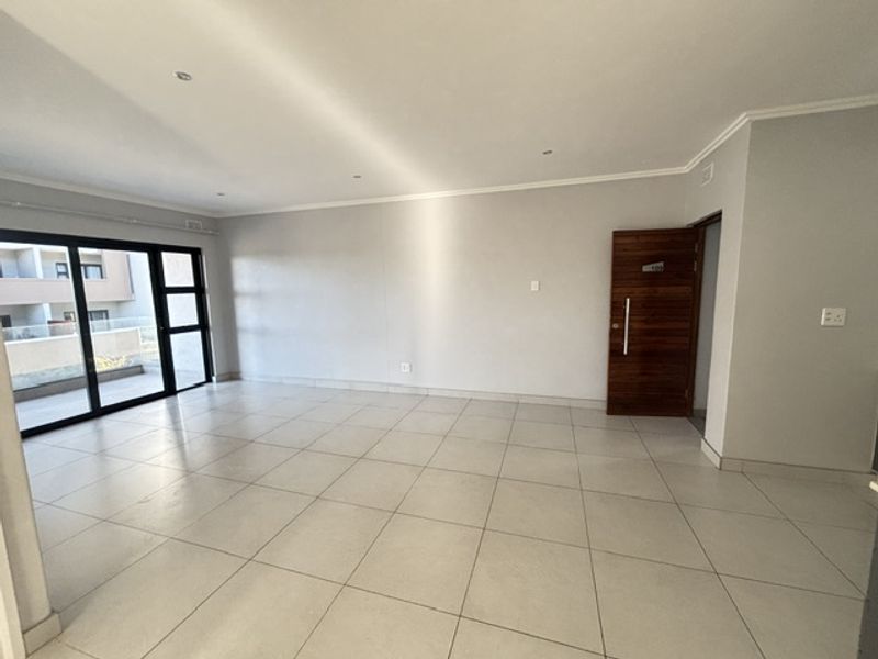 A spacious, empty living area featuring neutral tiled flooring, recessed lighting, and a large sliding glass door providing access to the balcony.