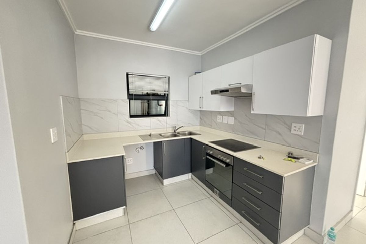 A modern, clean kitchen featuring two-tone cabinetry, stone countertops, integrated electric hob, oven, and extractor fan with neutral tiled flooring and backsplash.