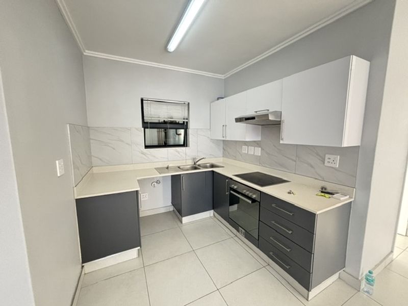 A modern, clean kitchen featuring two-tone cabinetry, stone countertops, integrated electric hob, oven, and extractor fan with neutral tiled flooring and backsplash.
