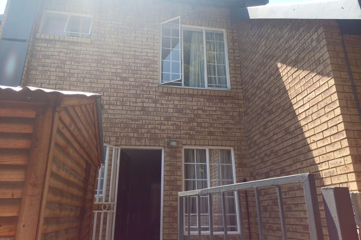 Rear view of a two-story townhouse featuring face brick construction, security gate access, and multiple casement windows.