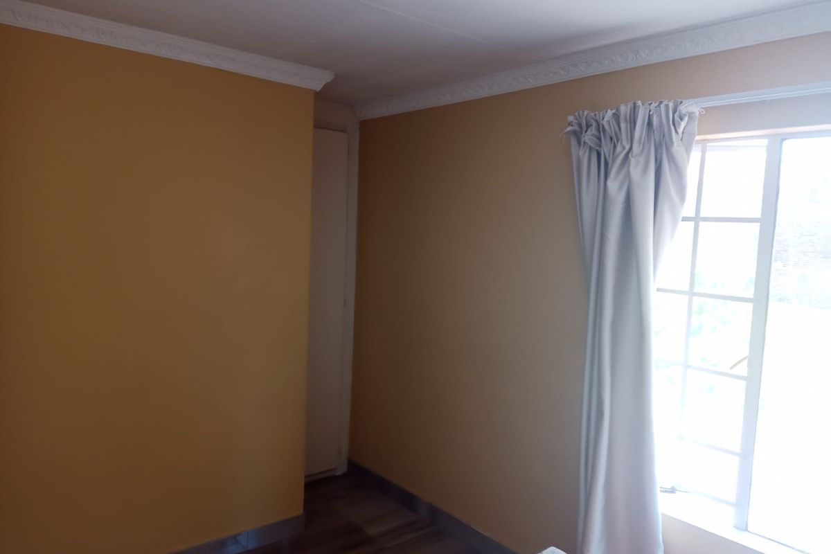 A vacant bedroom featuring laminated flooring, decorative cornice, and a window with security bars, offering a clean canvas for personalization.