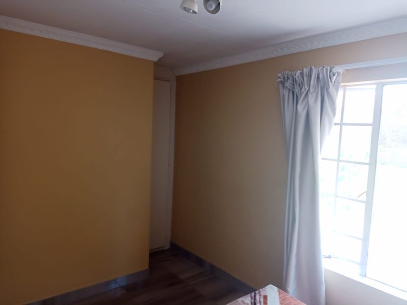 A vacant bedroom featuring laminated flooring, decorative cornice, and a window with security bars, offering a clean canvas for personalization.