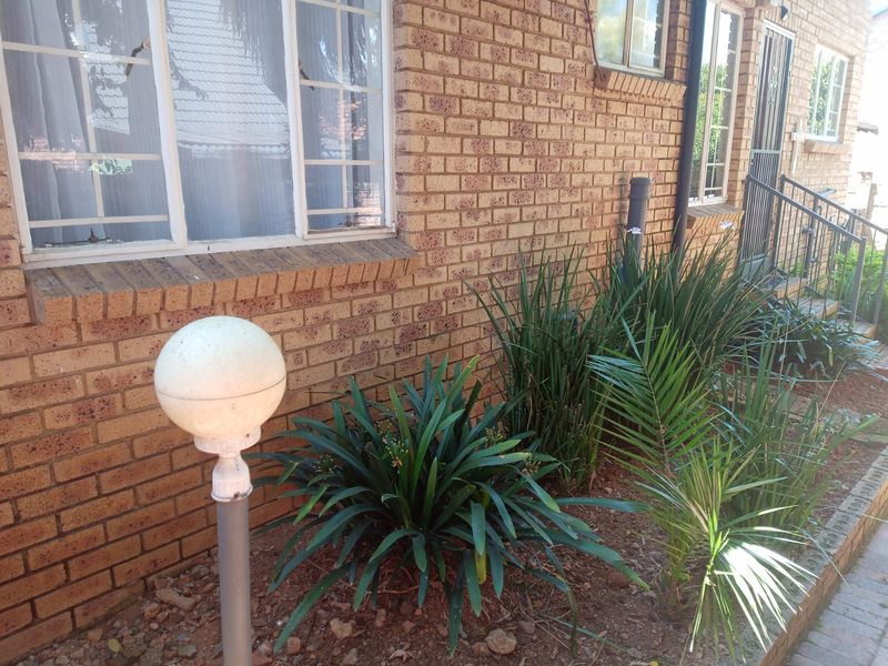 Front exterior view of the townhouse featuring face brick walls, security bars on windows, and a landscaped garden bed with a paved walkway.