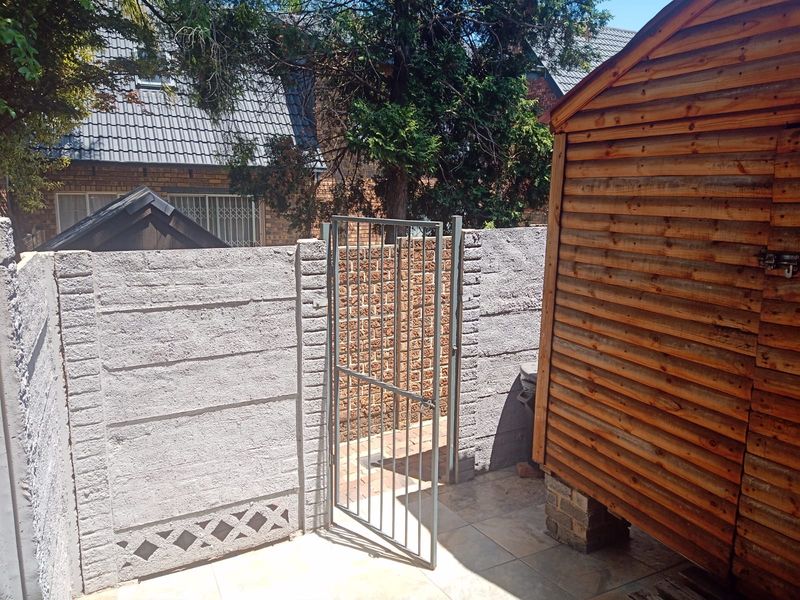A rear outdoor area featuring a tiled patio, a wooden garden shed, and a secure metal gate set within a precast concrete boundary wall.