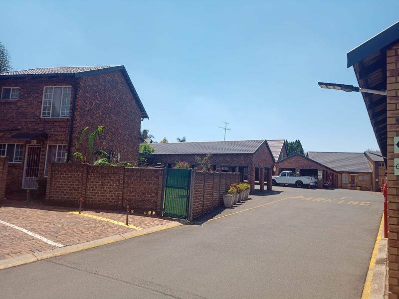 Exterior view of a face brick townhouse complex featuring paved driveways, secure boundary walls, and tiled roofing.