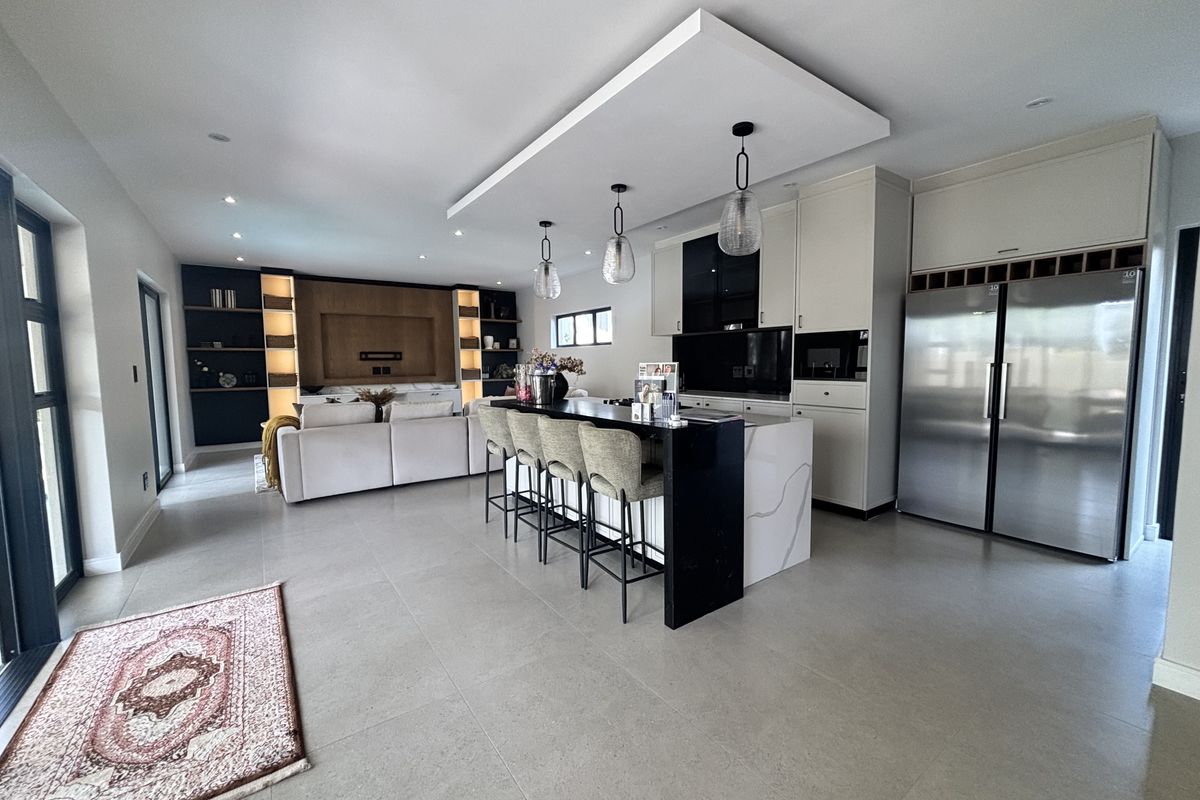 Modern open-plan living area featuring a sleek kitchen with a large island, stone countertops, integrated appliances, and custom built-in shelving in the lounge space.
