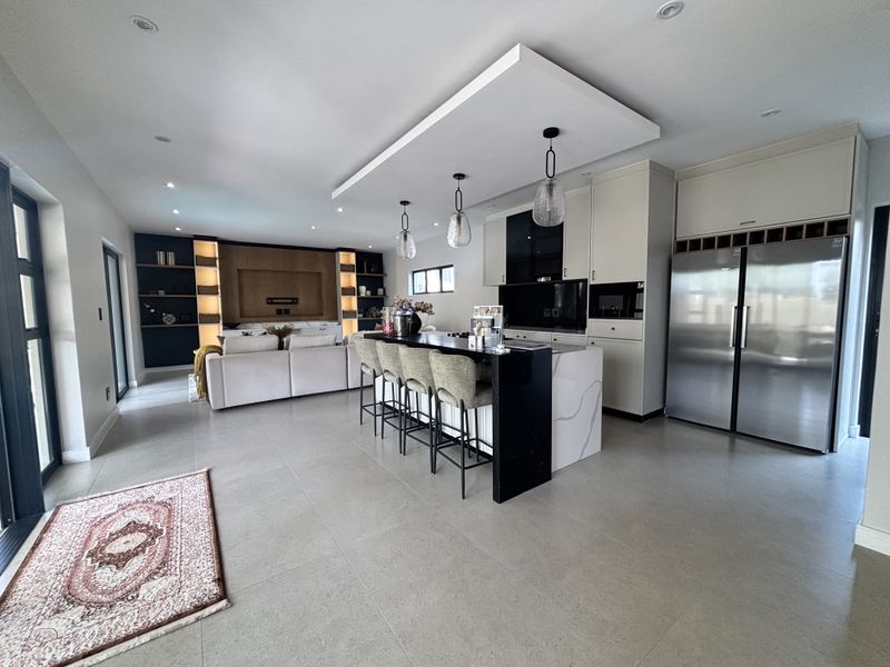 Modern open-plan living area featuring a sleek kitchen with a large island, stone countertops, integrated appliances, and custom built-in shelving in the lounge space.