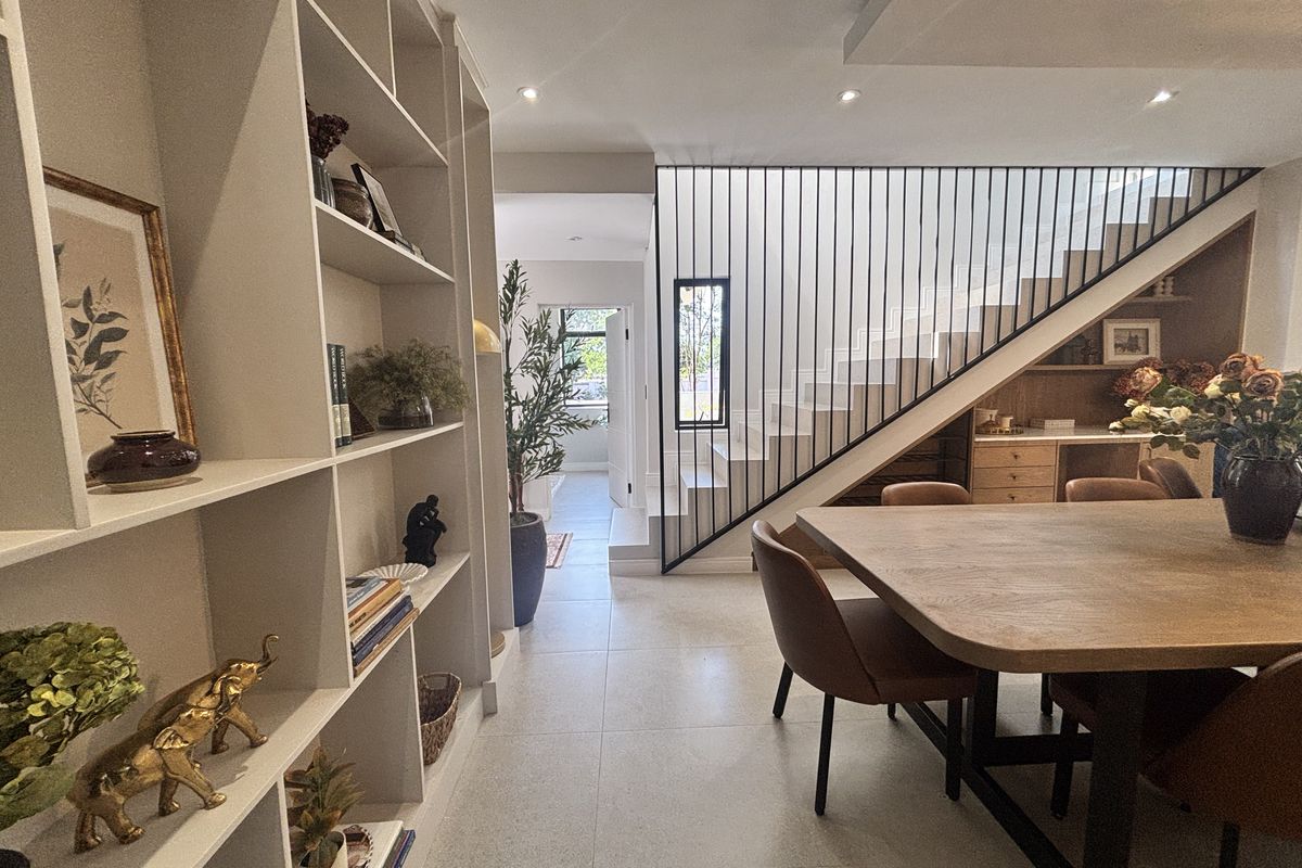 Modern living area featuring custom built-in shelving, a sleek staircase with metal balustrade, and integrated under-stair cabinetry with high-quality tiled flooring.