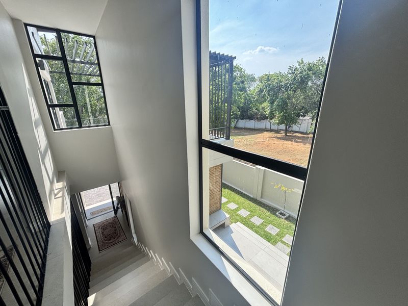 A bright, modern staircase landing featuring large windows that provide natural light and views of the garden and outdoor area.
