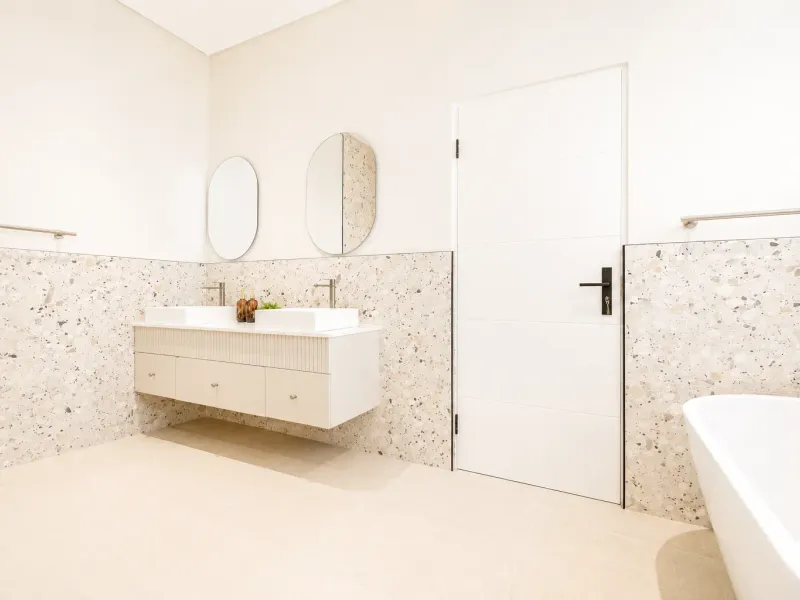 Modern bathroom featuring a double vanity with terrazzo wall tiling, a freestanding bathtub, and contemporary fixtures.