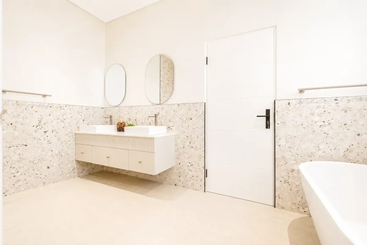 Modern bathroom featuring a double vanity with terrazzo wall tiling, a freestanding bathtub, and contemporary fixtures.