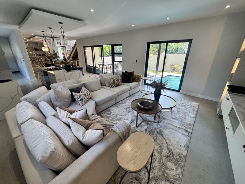 Spacious open-plan living area featuring a modern kitchen with stone island, seamless flow to the patio, and large sliding doors overlooking the pool.