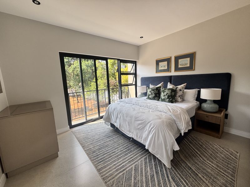 A well-maintained bedroom featuring neutral tiled flooring, recessed lighting, and a large sliding glass door providing access to an outdoor balcony area.