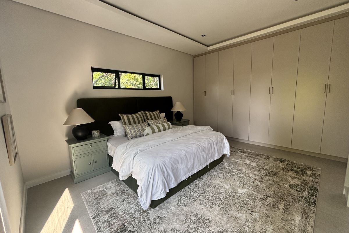 A modern, well-maintained bedroom featuring extensive built-in cupboards, a recessed ceiling with downlights, and a horizontal window providing natural light.