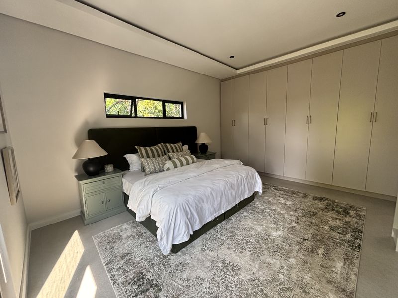 A modern, well-maintained bedroom featuring extensive built-in cupboards, a recessed ceiling with downlights, and a horizontal window providing natural light.