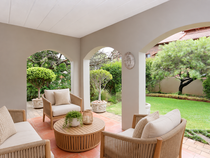 A charming covered patio featuring classic arched masonry openings, terracotta flooring, and direct access to a well-maintained private garden.