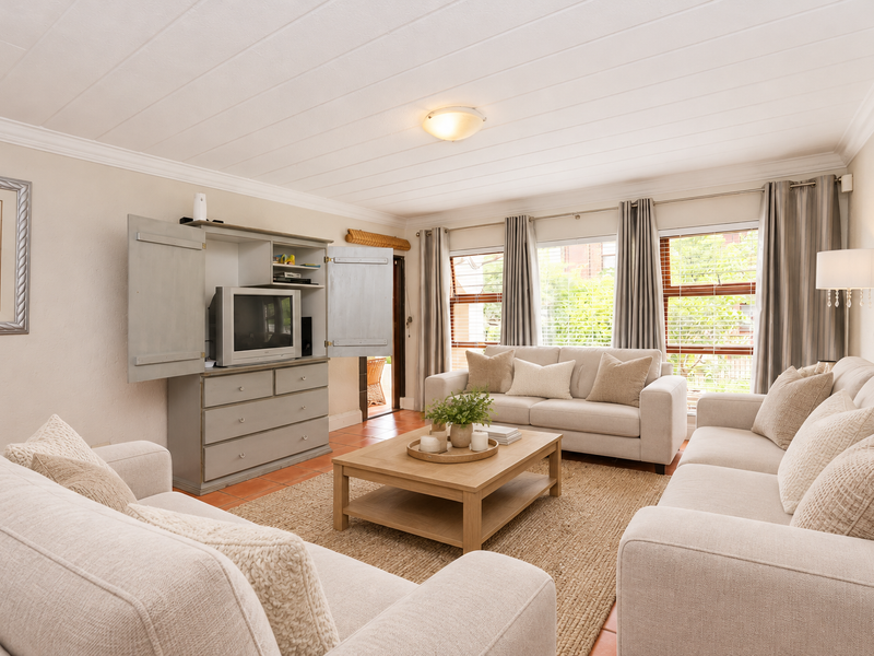 A bright and comfortable living room featuring tiled flooring, a panelled ceiling with crown moulding, and large windows that provide ample natural light.