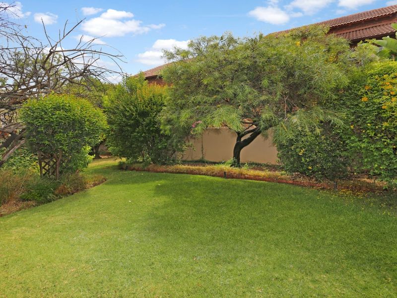 A well-maintained private garden area featuring a lush green lawn, mature trees, and established shrubbery enclosed by a boundary wall.