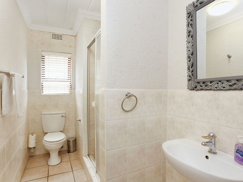A functional bathroom featuring a shower enclosure, wall-mounted basin, and tiled finishes, presenting an opportunity for cosmetic updates to modernize the space.