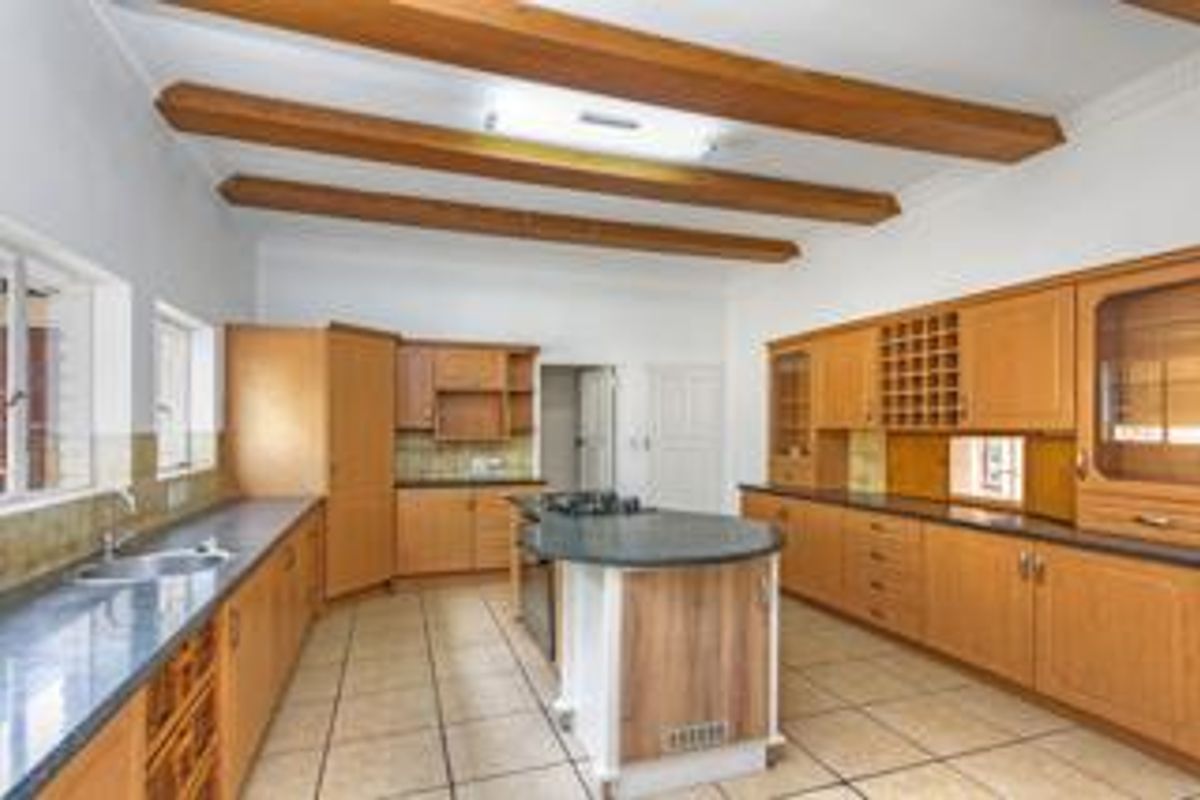 Spacious kitchen featuring exposed timber ceiling beams, extensive wooden cabinetry, a central island with a gas hob, and tiled flooring throughout.