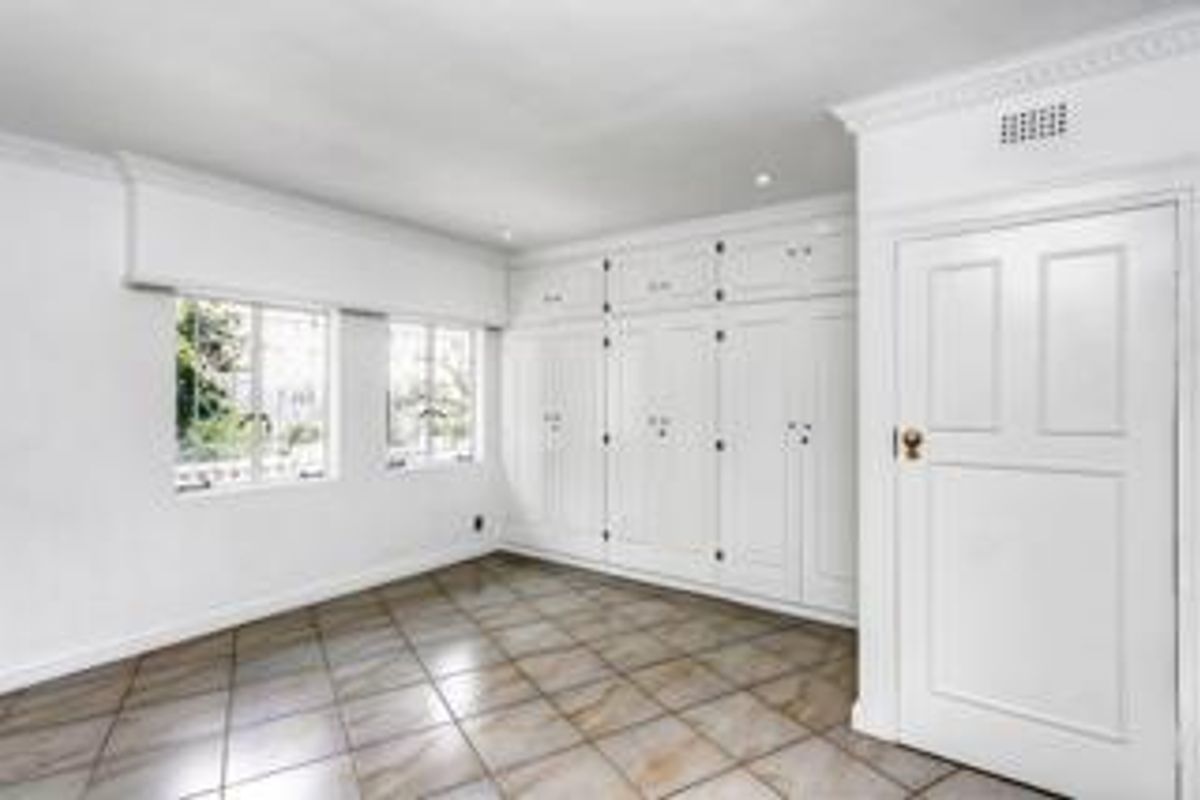 A bright, empty bedroom featuring extensive built-in white cabinetry, tiled flooring, and classic cornice detailing.