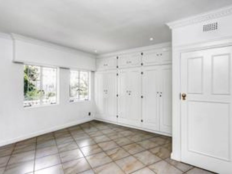 A bright, empty bedroom featuring extensive built-in white cabinetry, tiled flooring, and classic cornice detailing.
