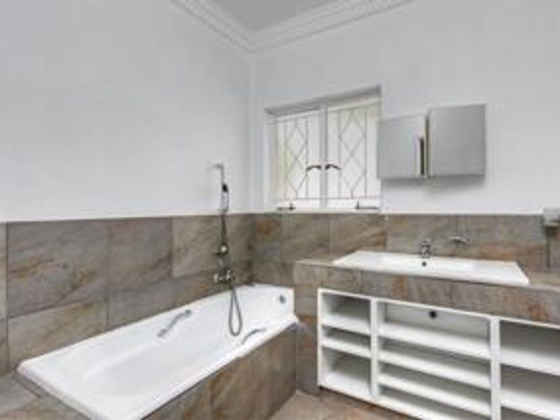 A clean, modern bathroom featuring a built-in bathtub, tiled surround, vanity basin with open shelving, and a mirrored medicine cabinet.