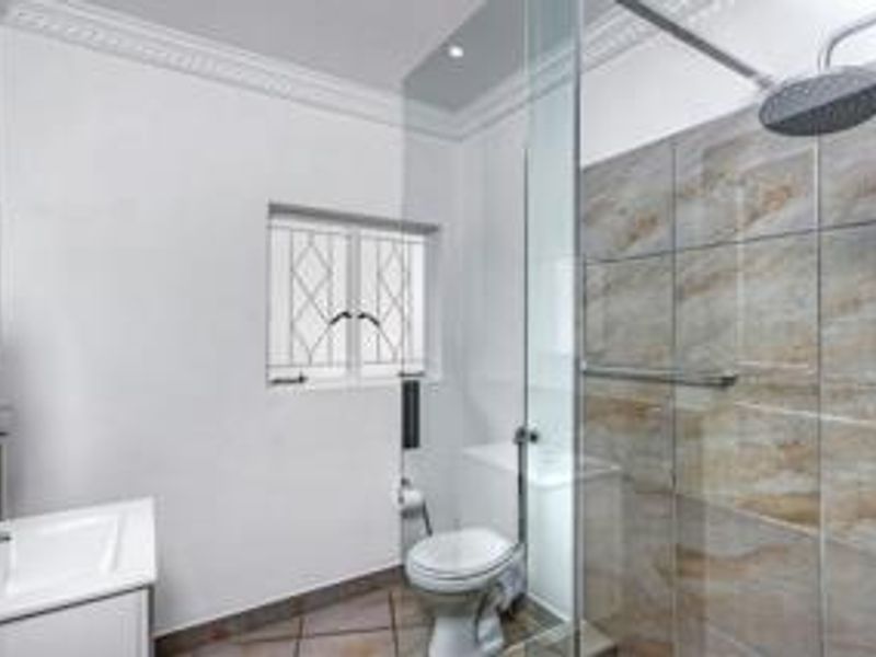 A modern, well-maintained bathroom featuring a walk-in shower with a rain shower head, a vanity basin, and tiled finishes.