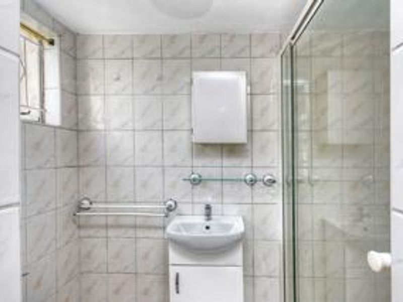 A functional bathroom featuring a shower enclosure, wall-mounted vanity basin, and tiled finishes, offering a clean and practical space.