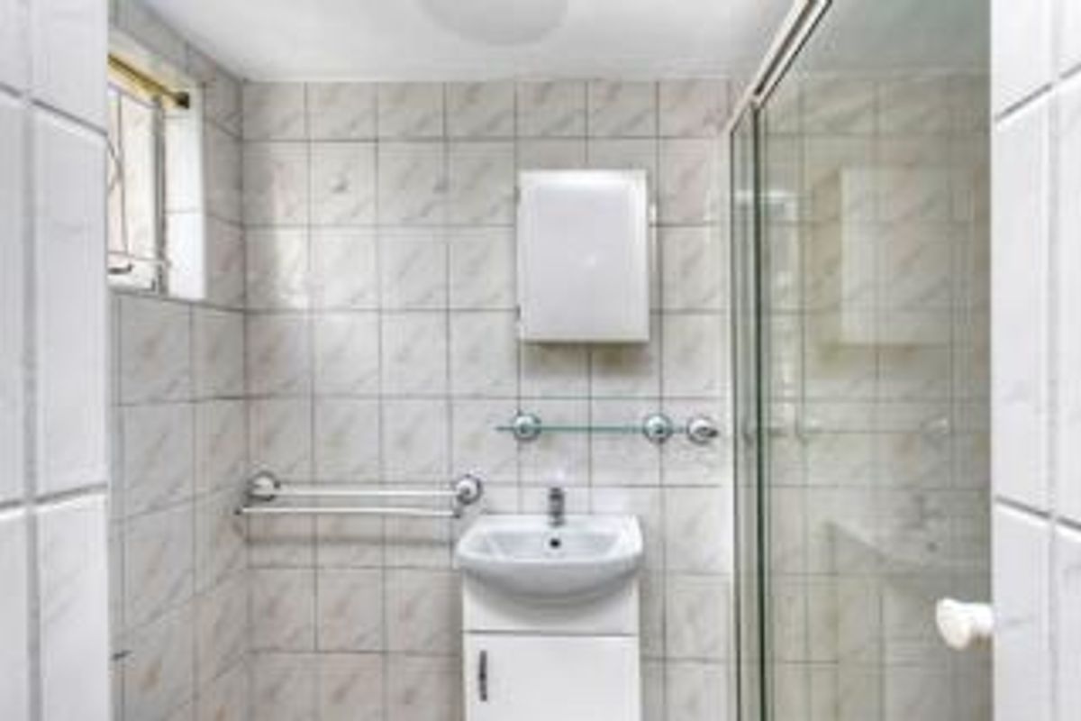 A functional bathroom featuring a shower enclosure, wall-mounted vanity basin, and tiled finishes, offering a clean and practical space.