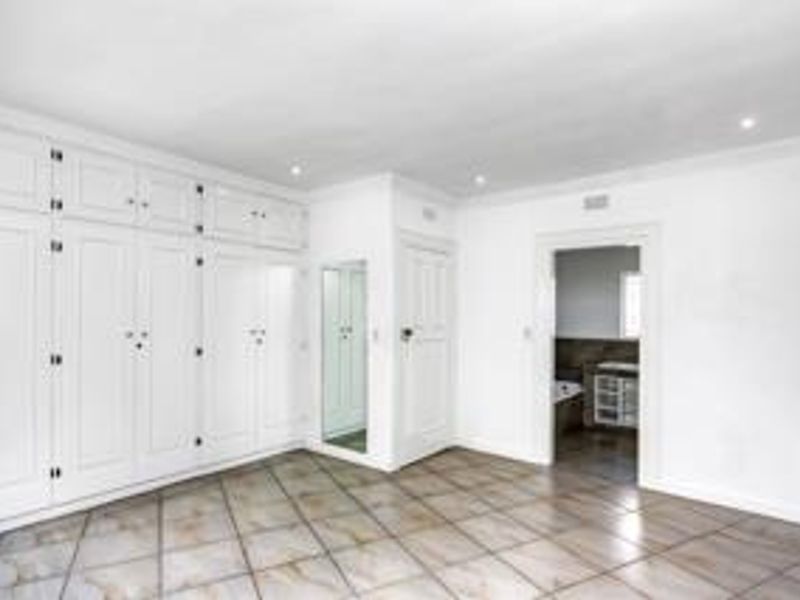 Spacious bedroom featuring extensive built-in cabinetry, tiled flooring, recessed lighting, and direct access to an en-suite bathroom.
