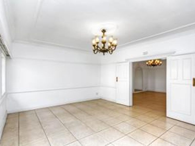 A bright, empty living room featuring tiled flooring, classic double doors, and a decorative ceiling rose with a chandelier.
