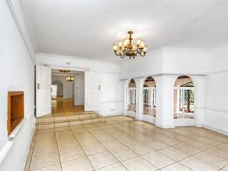 A spacious, empty living area featuring tiled flooring, elegant arched windows, and a raised platform leading to an adjacent room.