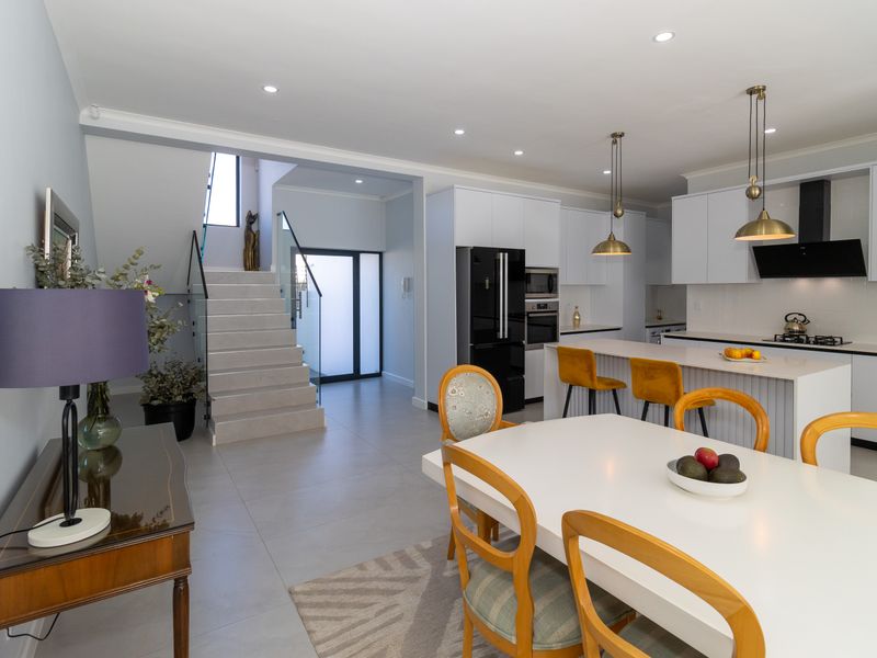 Modern open-plan living area featuring a sleek kitchen with island, built-in appliances, and a contemporary staircase with glass balustrade.
