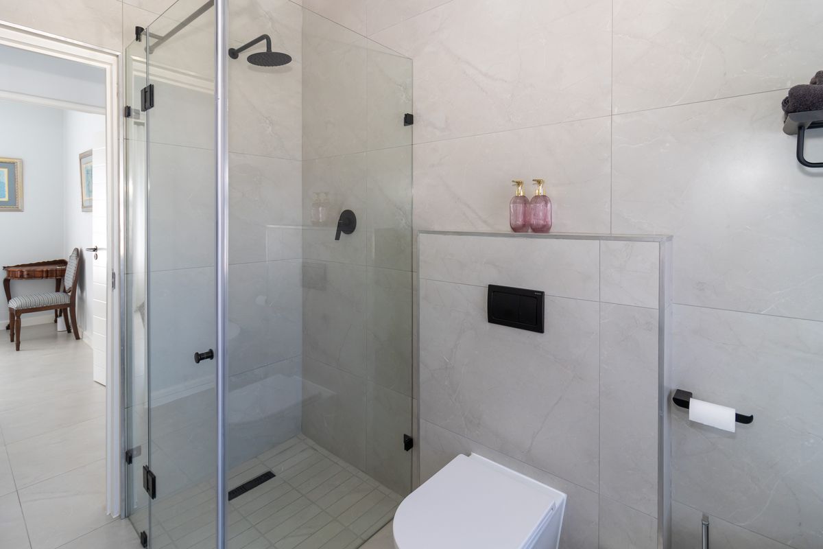 Modern bathroom featuring a walk-in shower with glass screen, rain shower head, and a wall-mounted toilet with concealed cistern, finished with neutral wall tiles.