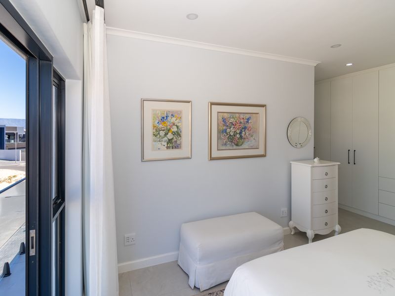 A bright and modern bedroom featuring built-in cupboards, recessed lighting, and a large sliding glass door providing access to an outdoor balcony area.