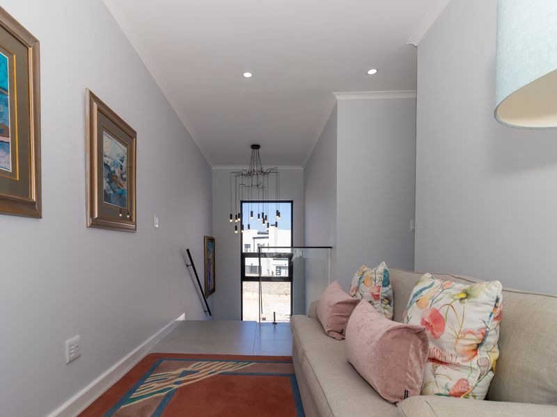 A bright and modern upper-level hallway featuring a contemporary chandelier, glass balustrade, and clean finishes leading towards a staircase.