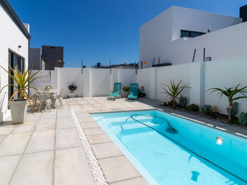 A well-maintained outdoor pool area featuring a paved patio, perimeter walls with electric fencing, and a clean swimming pool.