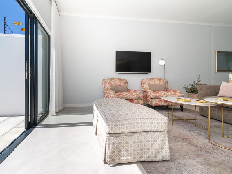 A bright and modern living room featuring large sliding glass doors that open to an outdoor area with electric security fencing.