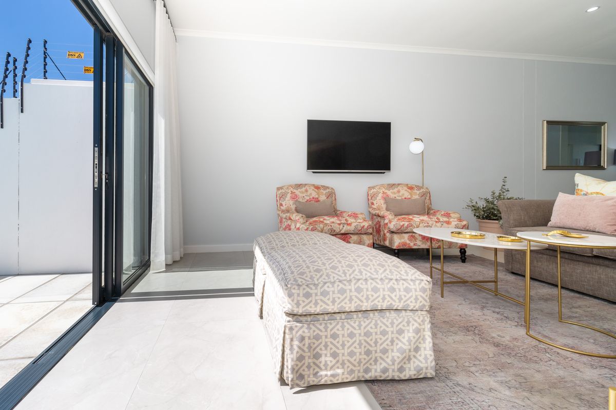A bright and modern living room featuring large sliding glass doors that open to an outdoor area with electric security fencing.