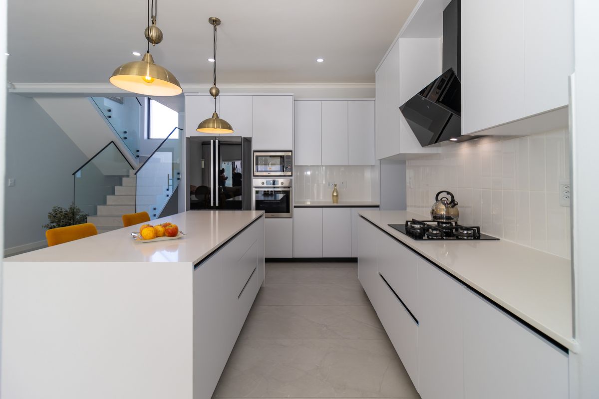 Modern kitchen featuring a large central island, quartz countertops, integrated appliances, and sleek white cabinetry, seamlessly flowing into the adjacent staircase area.