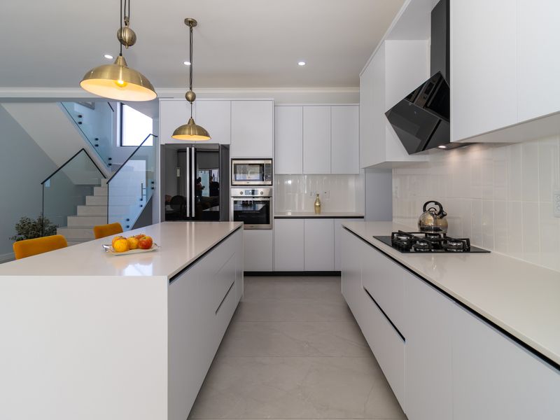 Modern kitchen featuring a large central island, quartz countertops, integrated appliances, and sleek white cabinetry, seamlessly flowing into the adjacent staircase area.