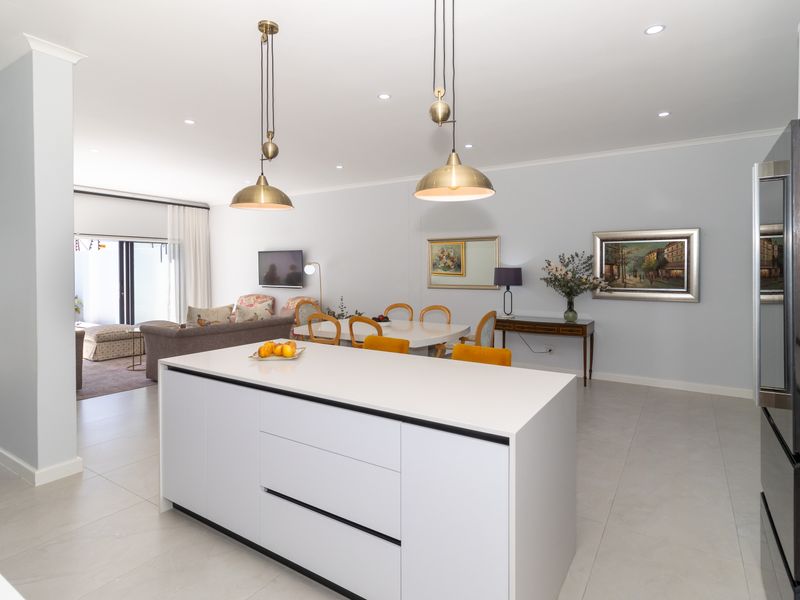 Spacious open-plan living and dining area featuring a modern kitchen island, sleek tiled flooring, and abundant natural light through sliding glass doors.