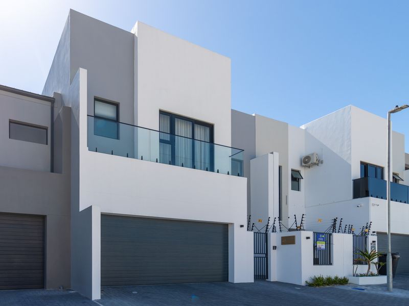 Modern double-story townhouse facade featuring a sleek grey and white exterior, glass balcony balustrade, and secure automated garage access.