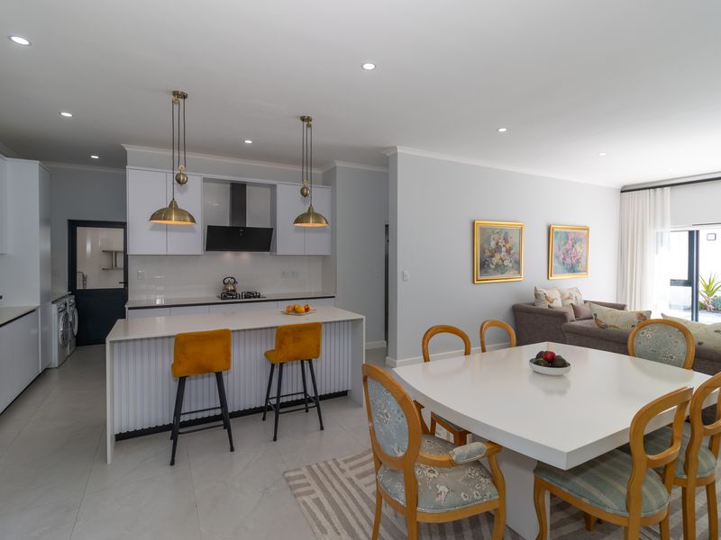 Modern open-plan living area featuring a sleek kitchen with a central island, integrated appliances, and seamless flow to the dining and lounge spaces.