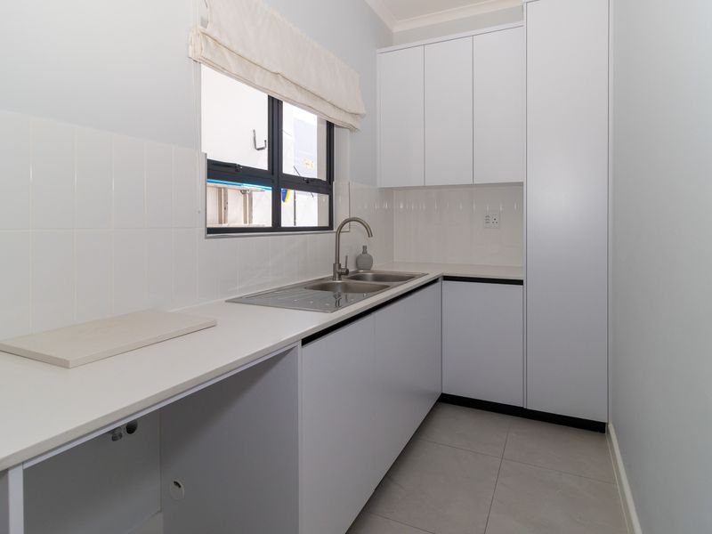 A clean and functional laundry room featuring white built-in cabinetry, a stainless steel sink, and neutral tiled flooring.