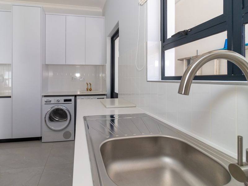 Modern laundry room featuring clean white cabinetry, a stainless steel sink with a mixer tap, and tiled flooring.